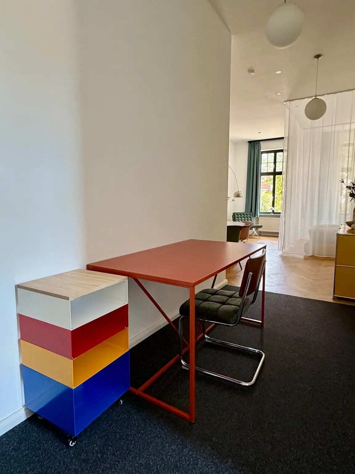 Heller Eingangsbereich der Bauhaus Suite mit rotem Schreibtisch und Blick in den Wohnraum
