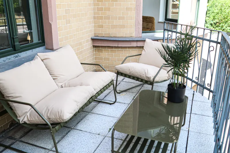 Balkon der Bauhaus Suite mit Loungesofa, Sessel, Glastisch und Palme im ruhigen Hof