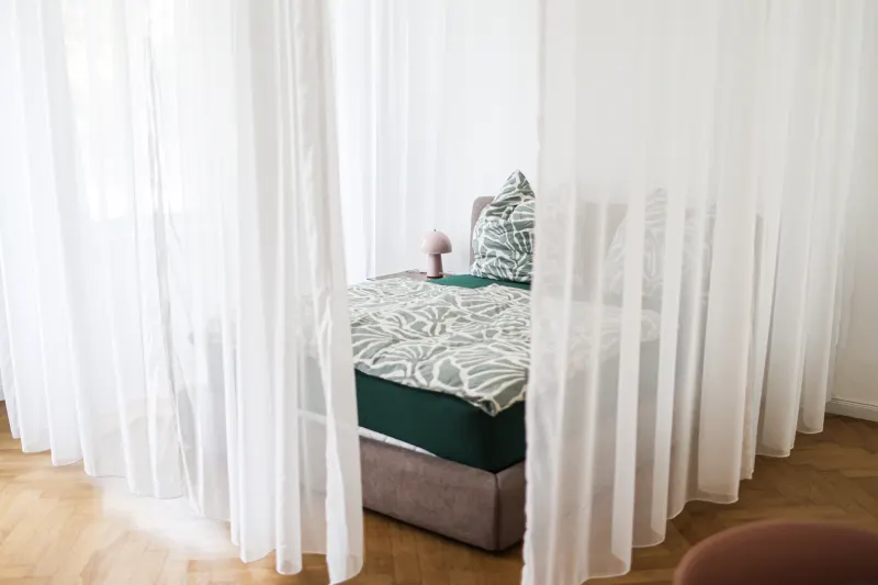 Doppelbett hinter blickdichten Vorhängen im abgetrennten Schlafbereich der Bauhaus Suite