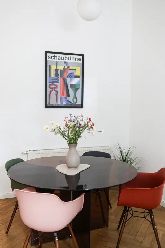 Runder Esstisch mit rosa, rotem und grünem Eames-Stuhl unter einem Bauhaus-Theaterplakat