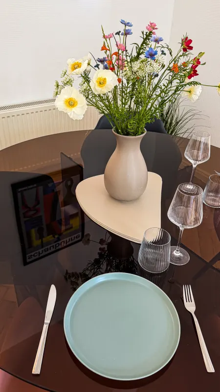 Detail des gedeckten Tisches mit türkisfarbenem Teller, Weingläsern und Wildblumenstrauß