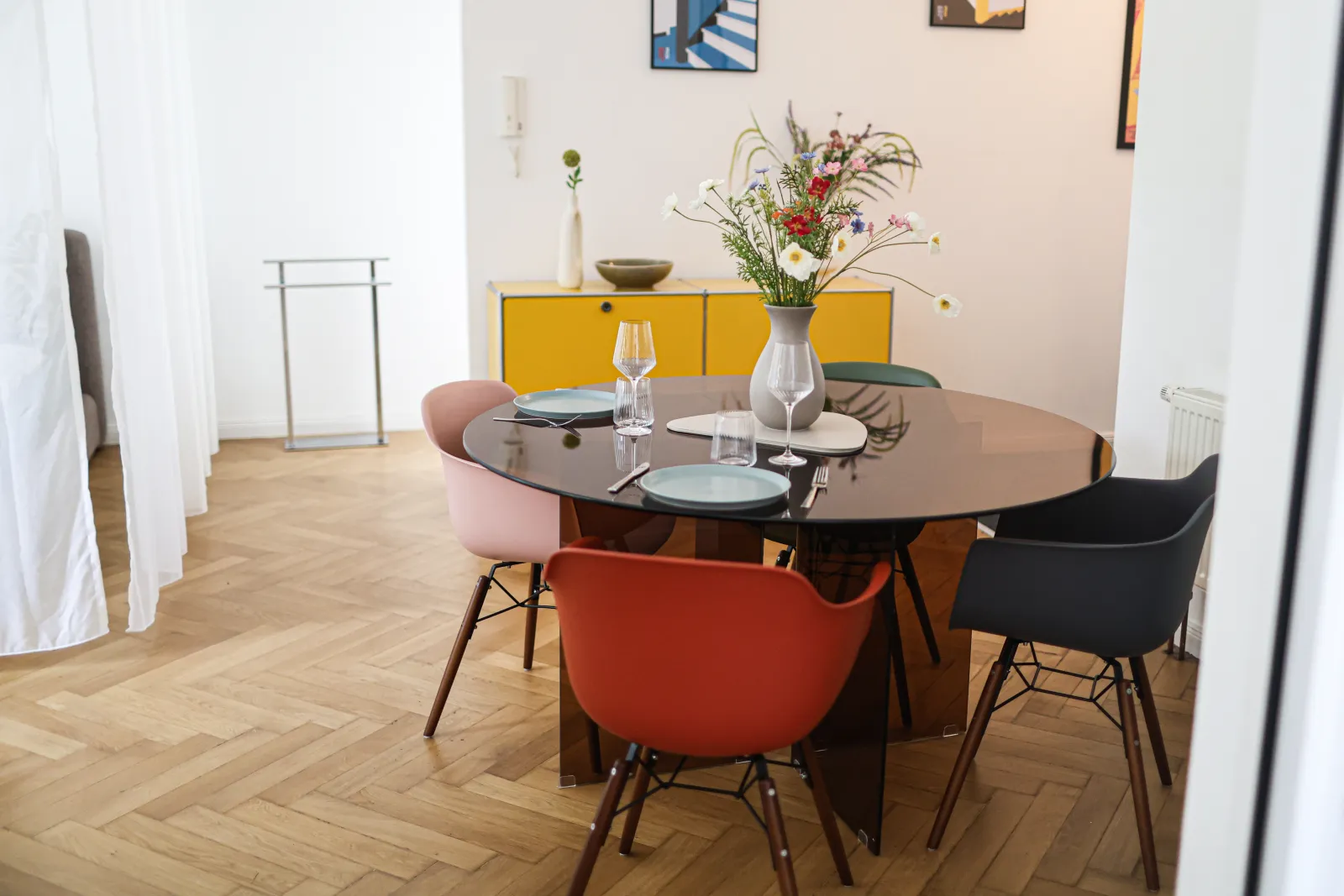 Heller Wohnraum der Bauhaus Suite mit rundem Esstisch, Eames-Stühlen, gelbem USM-Sideboard und Fischgrätparkett